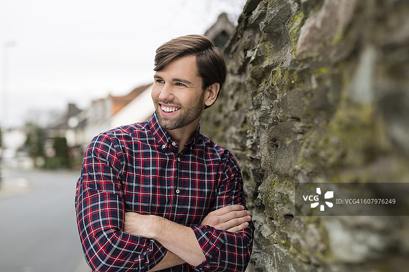 一幅微笑男子的肖像，穿着格子衬衫，靠在石墙上图片素材