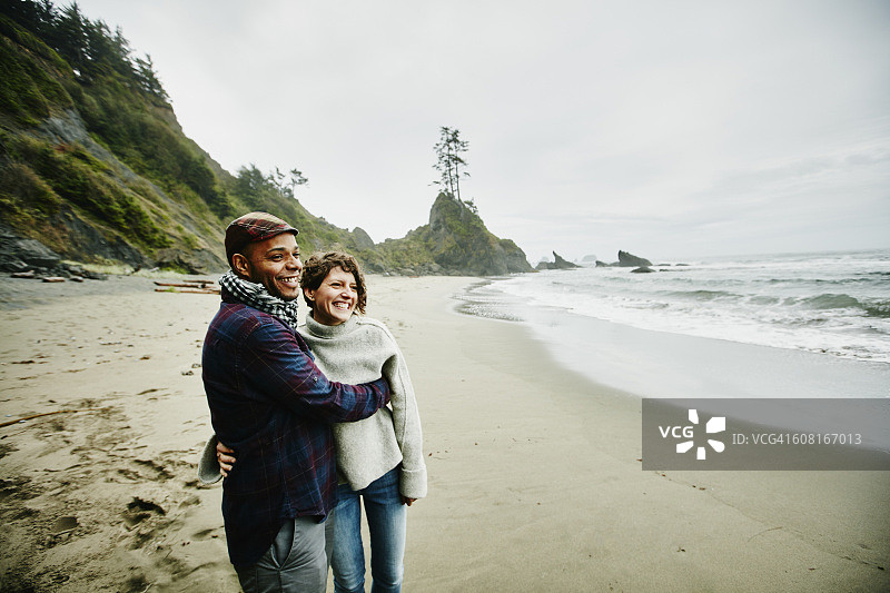 在秋天的早晨，一对笑嘻嘻的情侣在海滩上拥抱图片素材