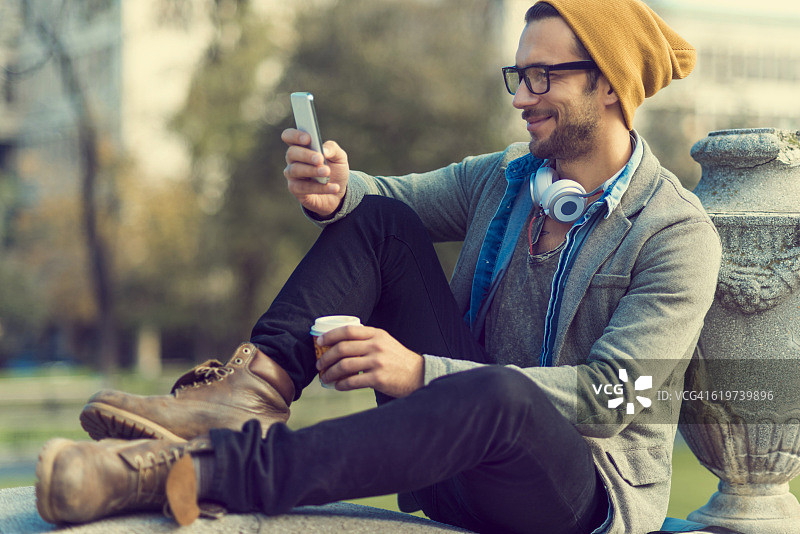 一个坐在公园里玩智能手机的帅哥图片素材