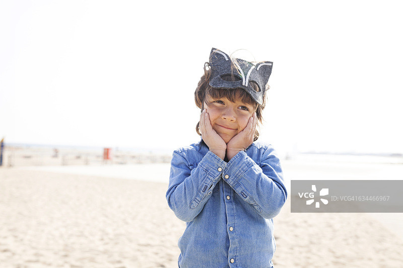 小男孩戴着动物面具在海滩上摆姿势做鬼脸图片素材