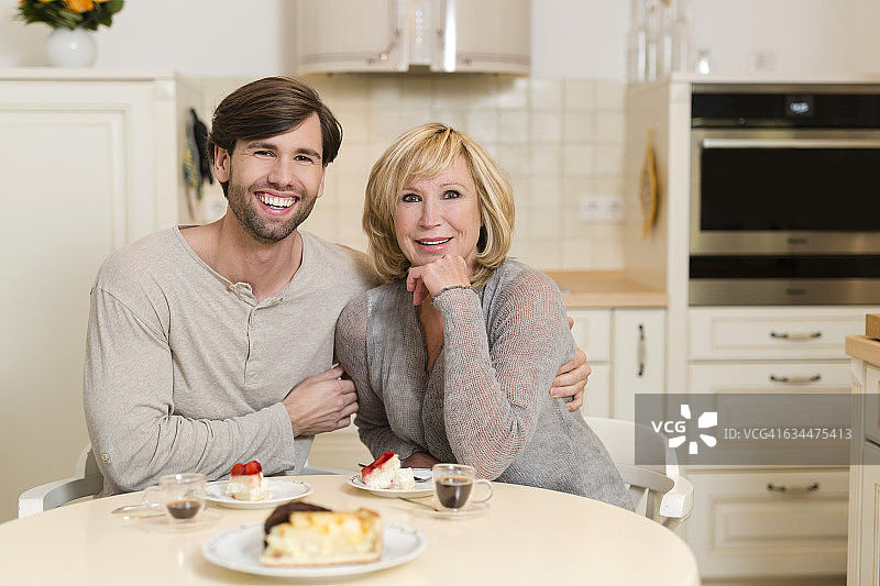 快乐的母亲和成年的儿子坐在厨房的桌子旁图片素材