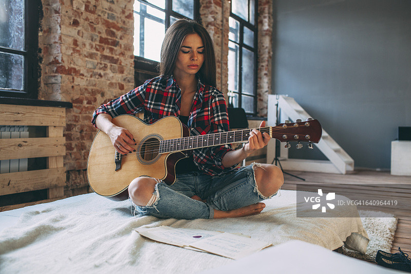 一个年轻女子坐在家里的床上弹吉他图片素材