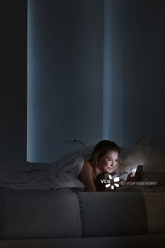 年轻女子晚上躺在床上看手机短信图片素材