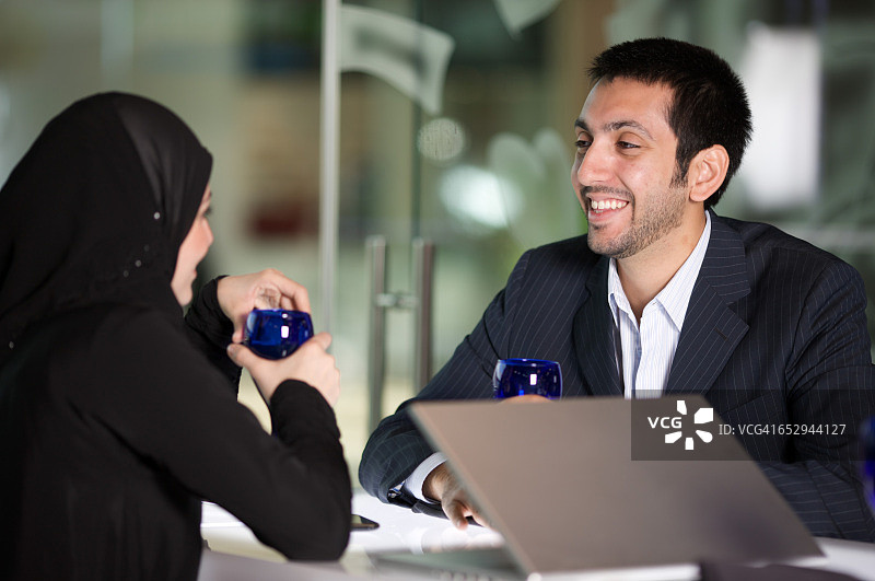 阿拉伯男人和女人在餐厅用餐并使用笔记本电脑。图片素材