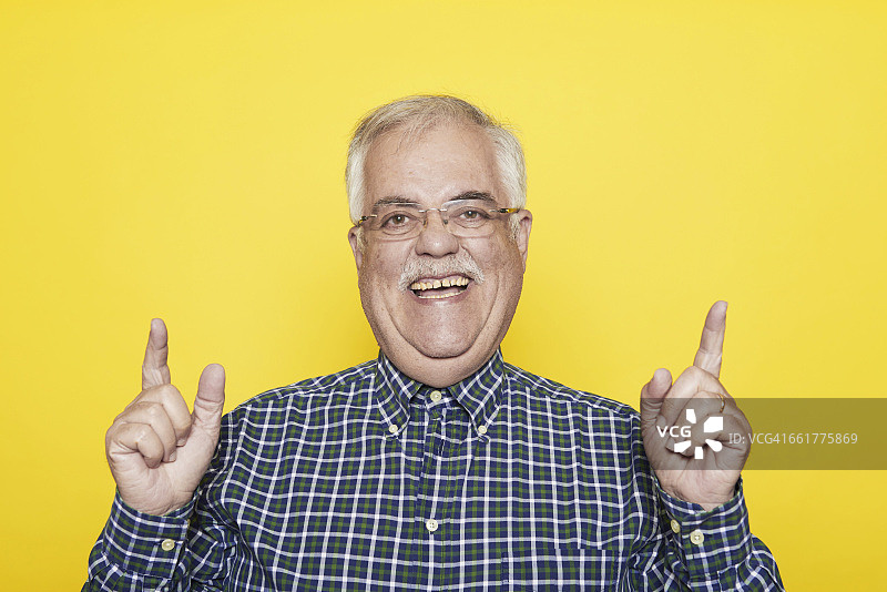一位在黄色背景前打手势的大笑老人的肖像图片素材