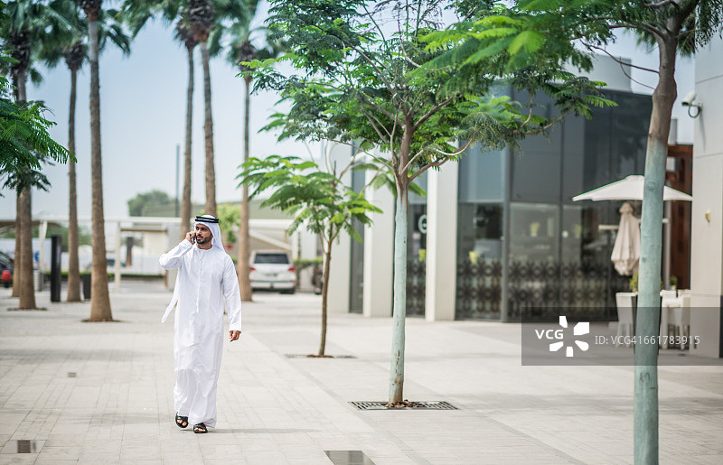 阿拉伯联合酋长国迪拜，一名穿着传统中东服装的男子走在街上用智能手机聊天图片素材