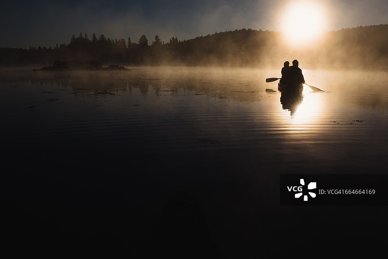 日落时分，一对老年夫妇在湖上划独木舟图片素材