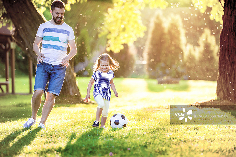 快乐的小女孩和她的父亲在公园踢足球图片素材