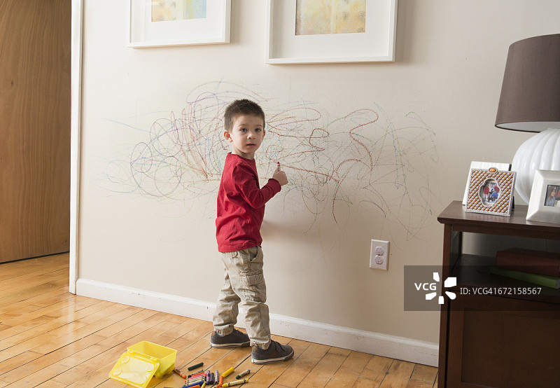 混血男孩用蜡笔在墙上画画图片素材