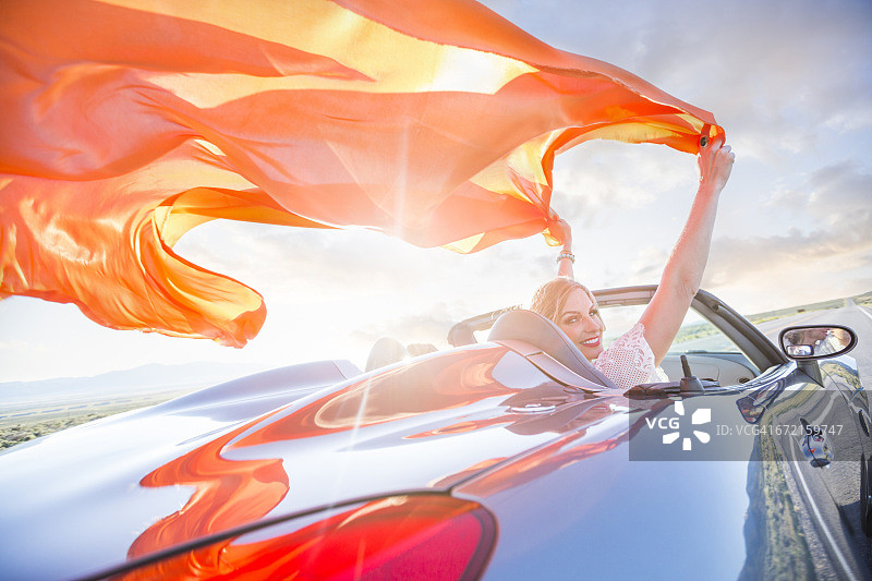 白人女人在风中拿着橙色的织物在跑车里图片素材