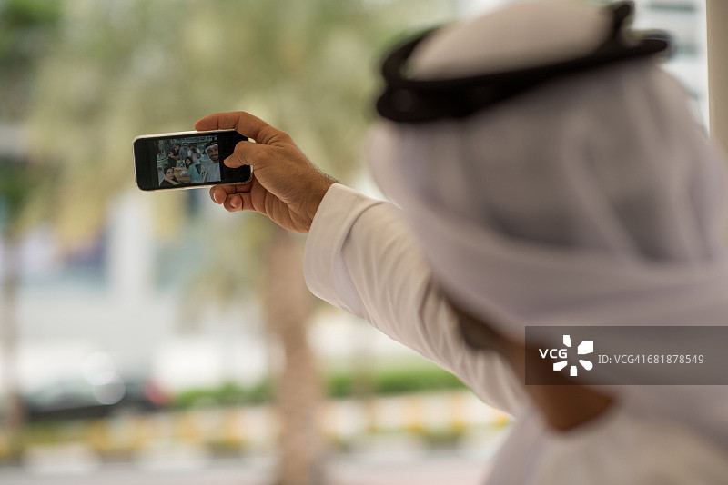 阿拉伯联合酋长国迪拜，一名中东男子在咖啡馆用智能手机与朋友自拍图片素材