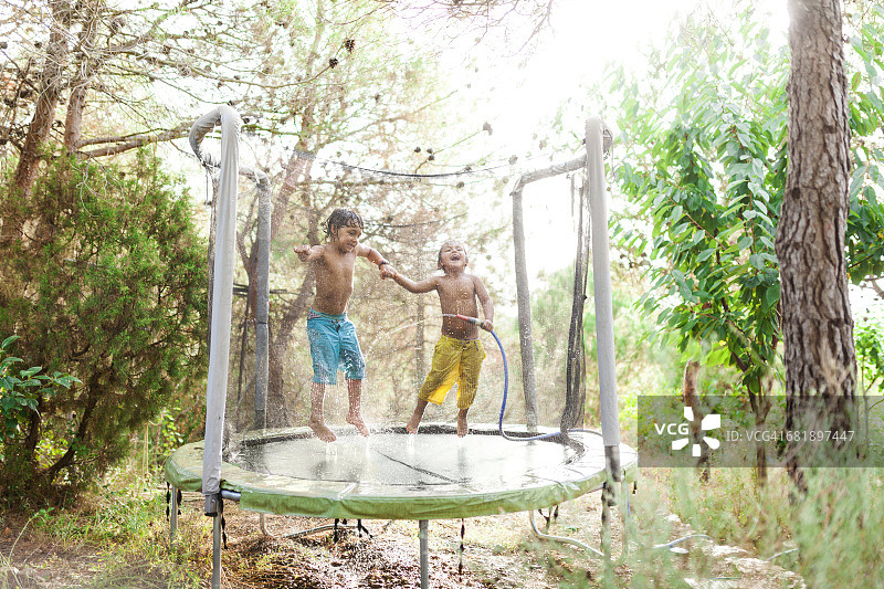 两个小男孩在蹦床上跳着，同时用花园软管泼水图片素材