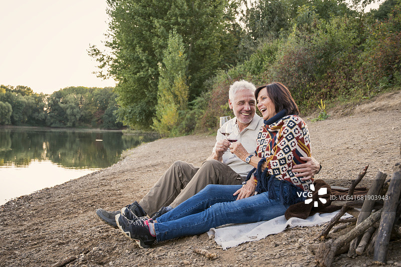 快乐的老年夫妇在晚上的湖边喝着酒图片素材