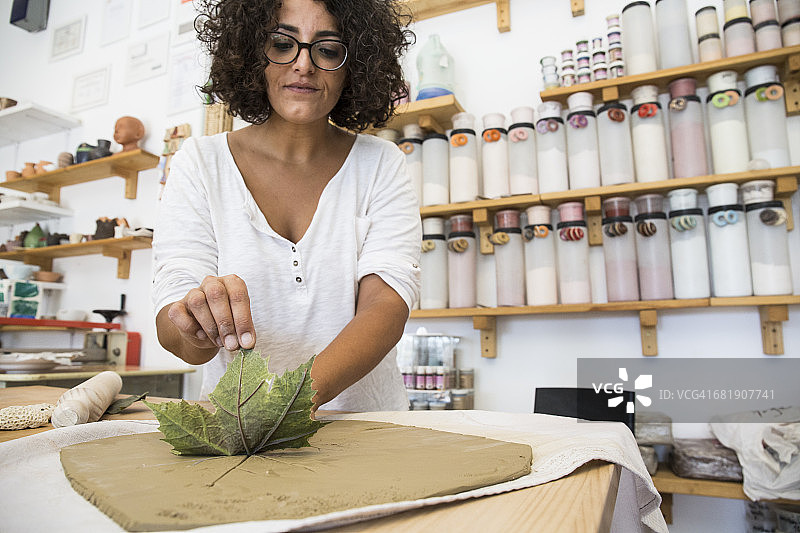 在陶艺作坊里，一名妇女正在用一片叶子印一幅陶土画图片素材