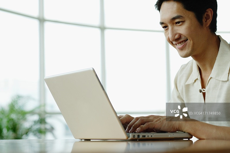 男人坐着，用着笔记本电脑，微笑着图片素材