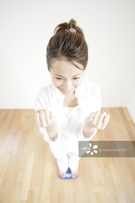高角度的观点，一个年轻的女人站在一个秤上，使拳头图片素材