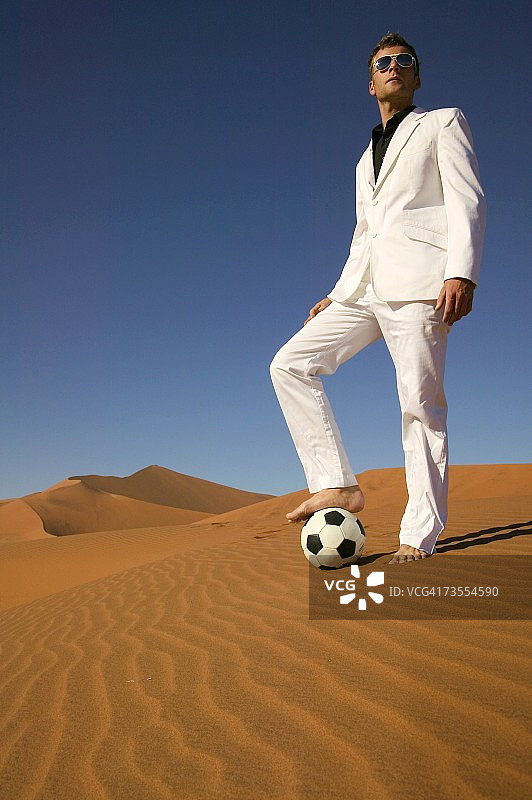沙漠中一个穿着白色西装的人站在足球上图片素材