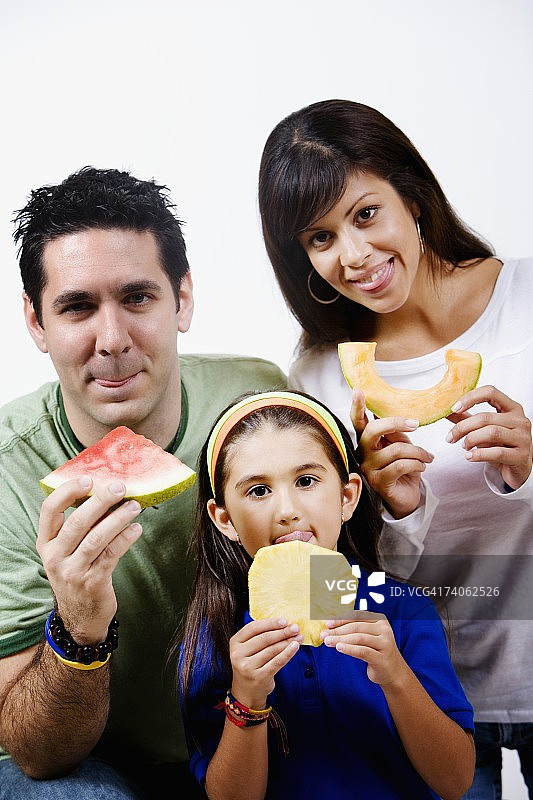 年轻女子和一个中年男子和他们的女儿拿着水果片，伸着舌头图片素材