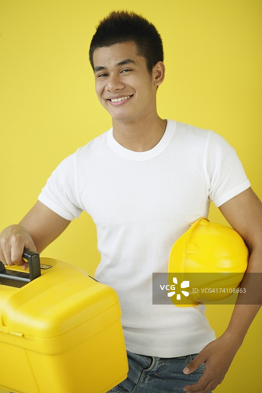 男人拿着建筑帽和工具箱，对着镜头微笑图片素材