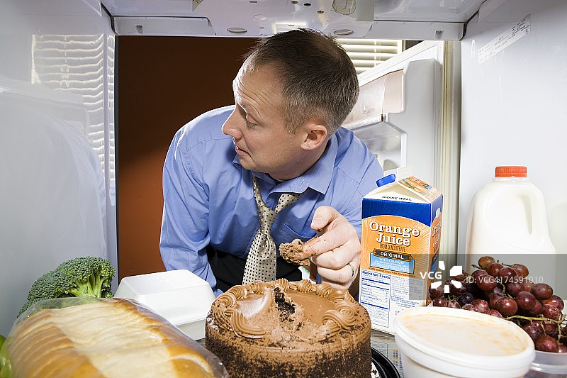 冰箱里的男人从巧克力蛋糕上取糖霜图片素材