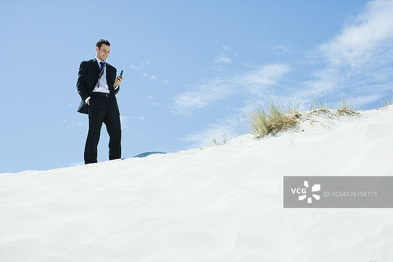 商人站在沙丘上，低头看手机图片素材
