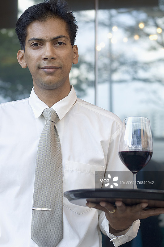 一个中年男子用托盘端着一杯红酒的肖像图片素材