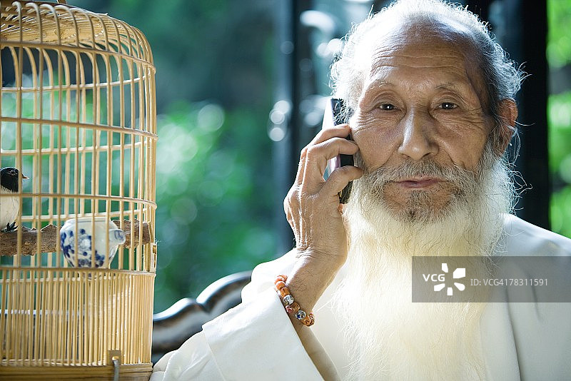 老人穿着中国传统服装，用手机，旁边放着鸟笼图片素材