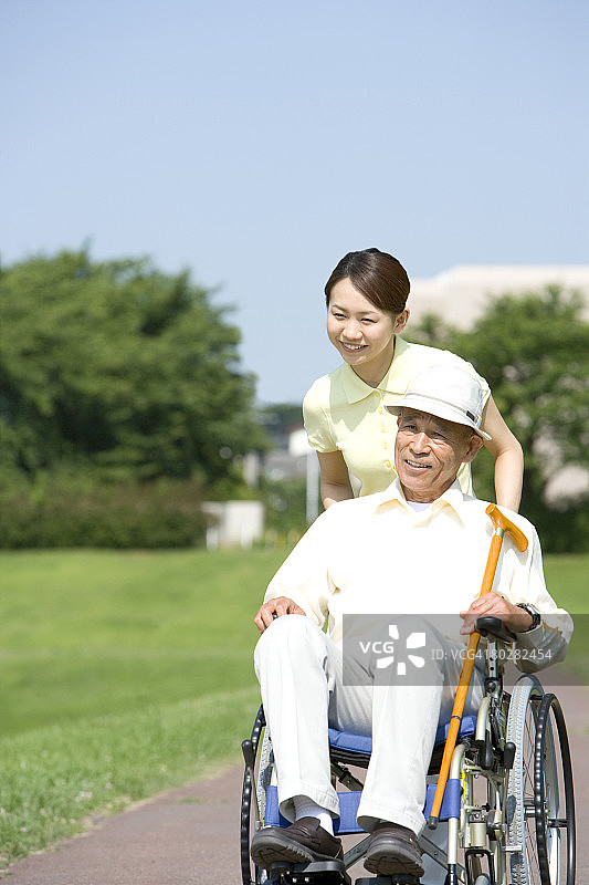 女护士推着轮椅上的老人，面带微笑，目光分散图片素材