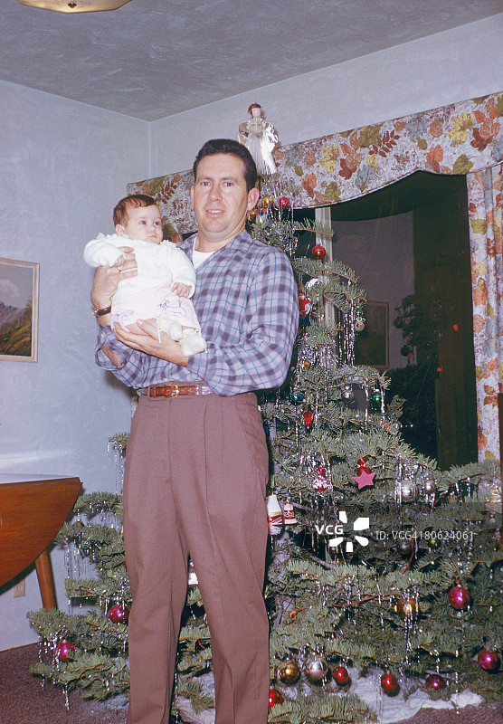 父亲抱着孩子站在圣诞树前图片素材