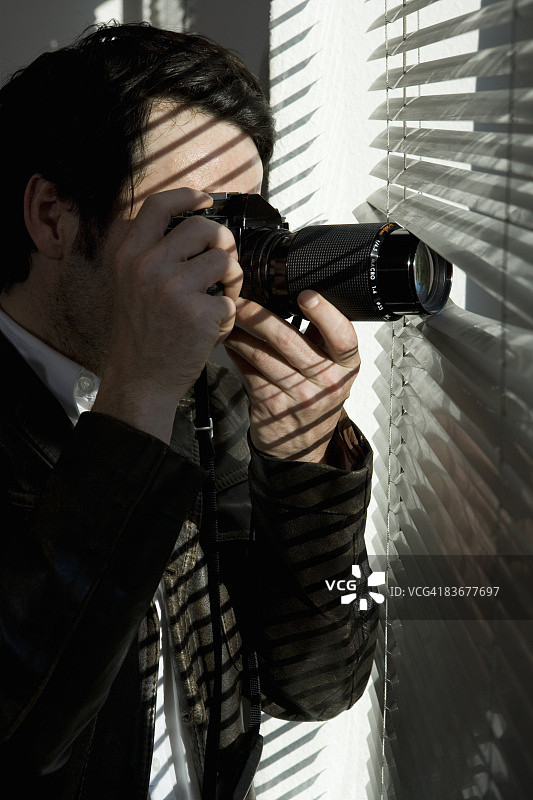 一个拿着相机透过百叶窗看的男人图片素材