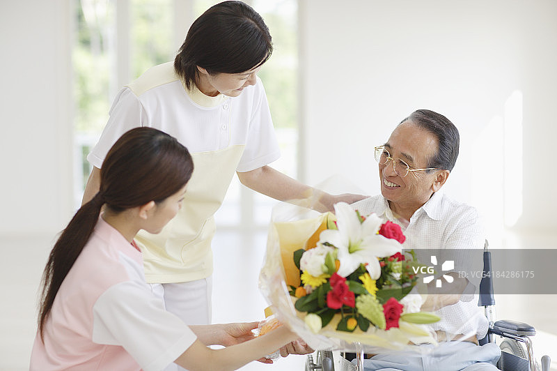 护理人员向坐在轮椅上的老人献上一束鲜花图片素材