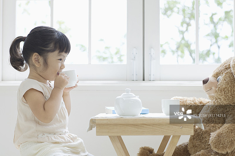 女孩在和泰迪熊喝茶休息，侧视图图片素材