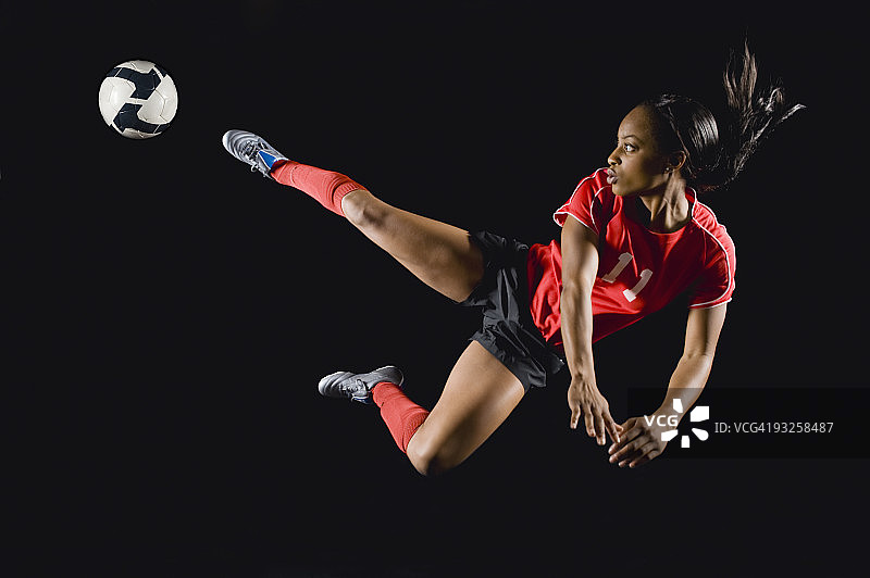混合种族足球运动员在半空中踢足球图片素材