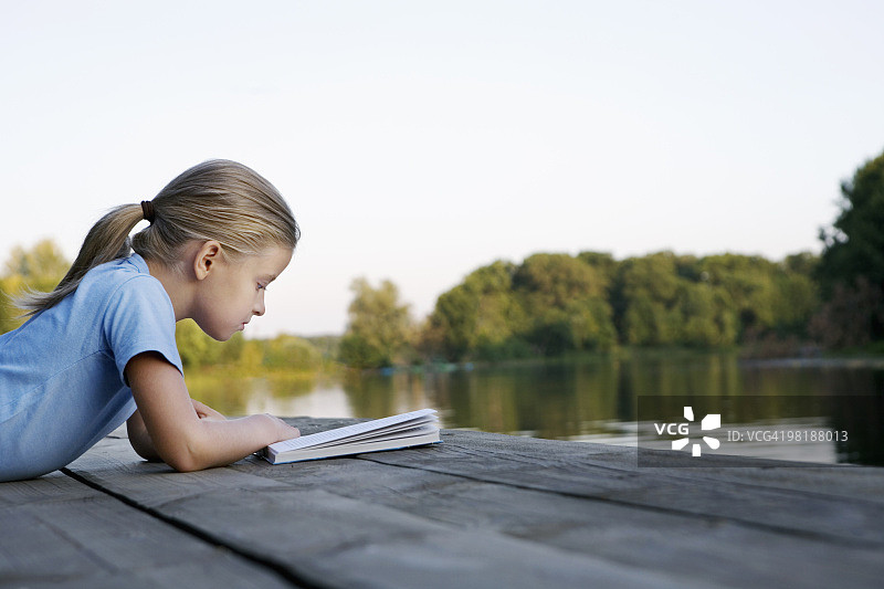 一个小女孩在一个木制的防波堤上看书图片素材