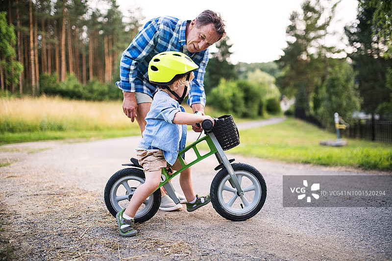 一个蹒跚学步的小男孩和他的祖父在户外骑着平衡自行车。图片素材