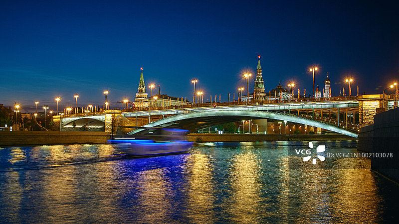 夜晚灯火通明的莫斯科克里姆林宫全景。前方的莫斯科大剧院桥下，游船在莫斯科河上航行。图片素材