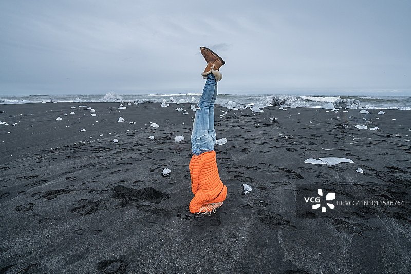 年轻女子头倒立瑜伽姿势在黑沙滩附近的冰和海在冰岛图片素材