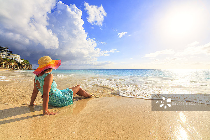 戴着帽子和穿绿松石衣服的女人坐在海边看绿松石加勒比海，弗里斯海滩，安提瓜岛图片素材