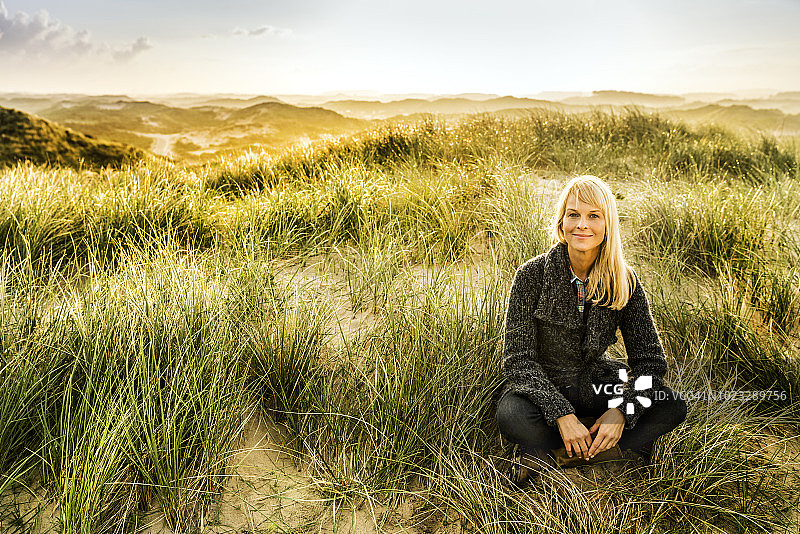 一个微笑的女人坐在沙丘上的肖像图片素材