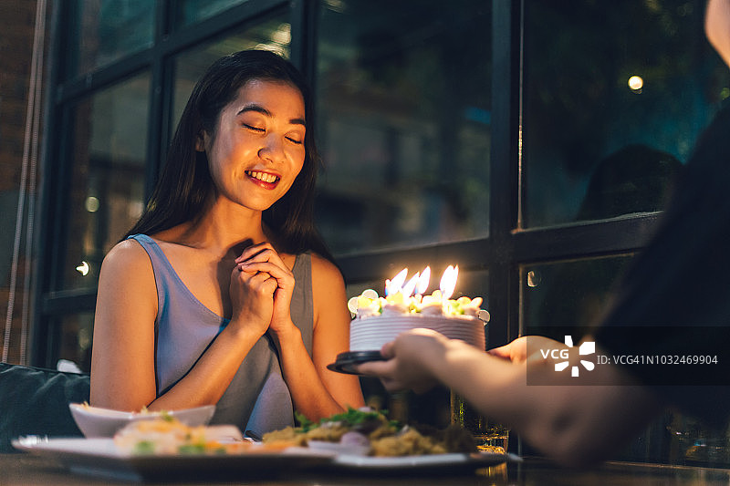 亚洲妇女在幸福之夜从她的生日蛋糕祈祷。图片素材