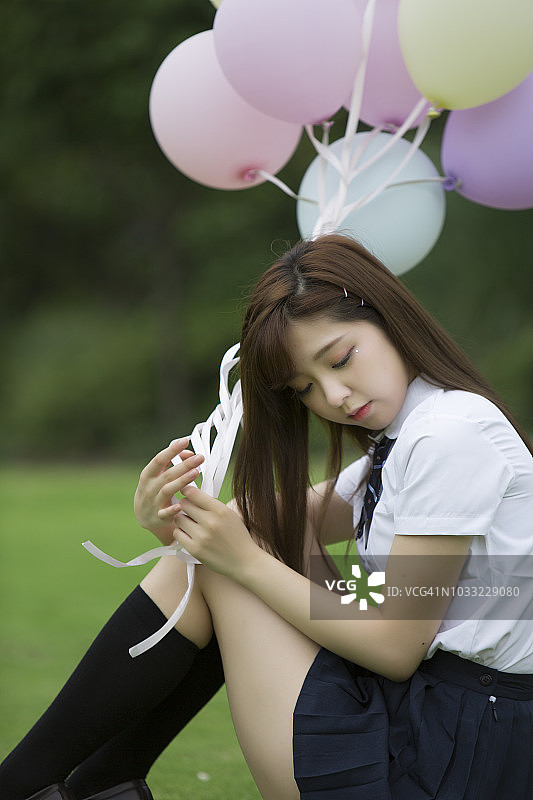 夏天五颜六色的气球。年轻的成年亚洲女孩的肖像拿着一束彩色气球坐在绿色的草地上图片素材