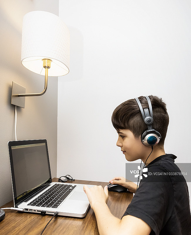 一个小男孩在家里的一张小桌子上做作业，同时听着耳机图片素材
