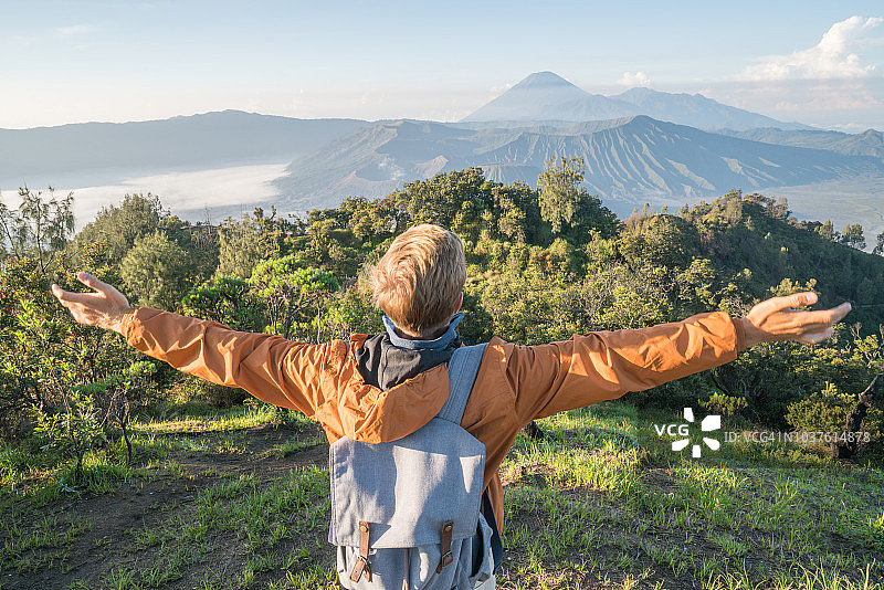 在印度尼西亚，年轻人徒步旅行，手臂伸开站在火山的山顶上，人们旅行的乐趣，冒险的概念，成功和成就图片素材