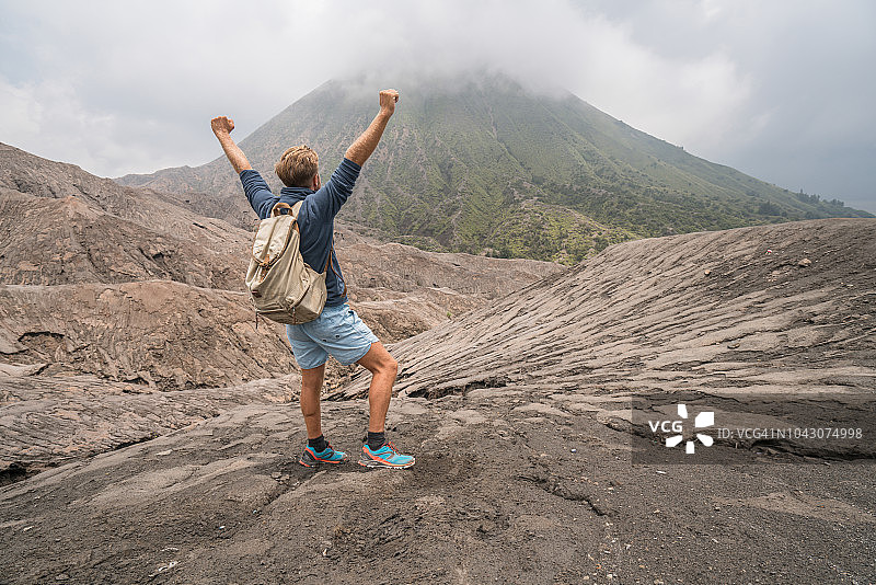 年轻人徒步站在火山上伸出手臂与Bromo火山在印度尼西亚的观点-人们旅行有趣的冒险概念成功和成就图片素材
