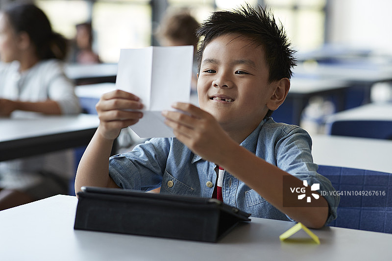 男孩微笑着读着纸条，坐在教室里图片素材