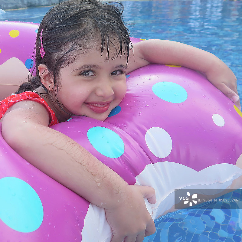 4岁的女孩度假在游泳池游泳与粉红色的充气环。图片素材