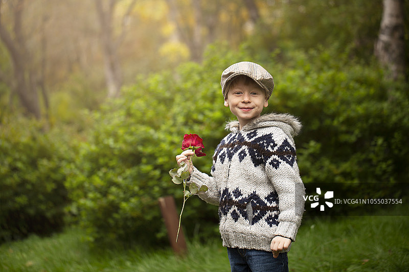 公园里微笑的男孩抱着玫瑰的肖像图片素材