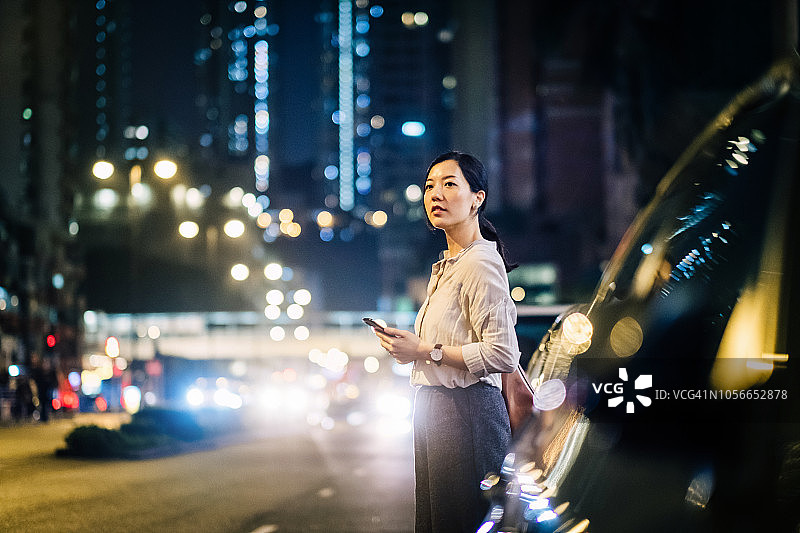 一名年轻的亚洲女子在市中心街道上用智能手表上的手机应用安排出租车，背景是模糊的交通场景图片素材