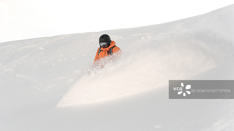身穿橙色运动服的职业滑雪板运动员在白色天空的映衬下从山坡上滑下来图片素材