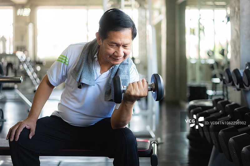 亚洲老人在健身房用哑铃锻炼。图片素材